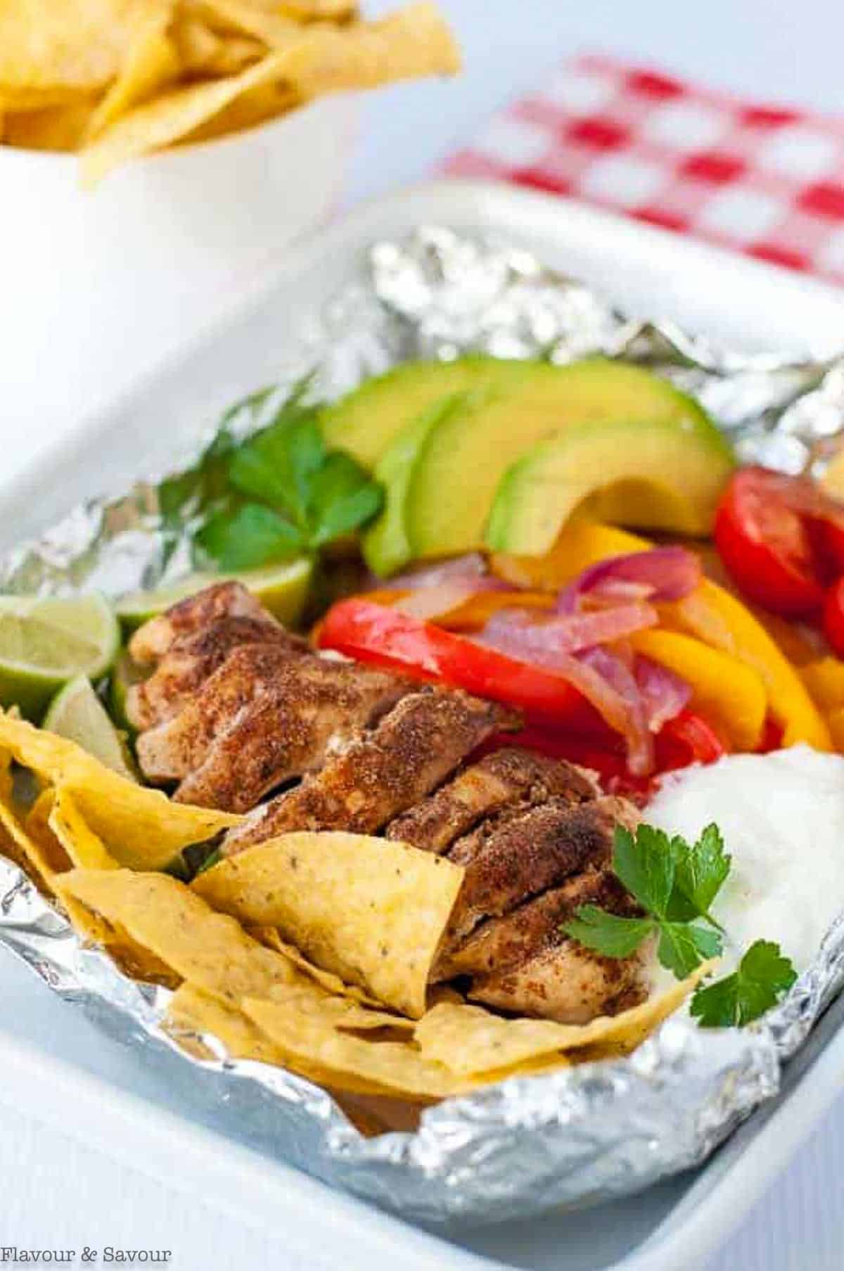 a foil packet with fajita chicken breast, sliced peppers, onions, avocado, tomatoes, and tortilla chips