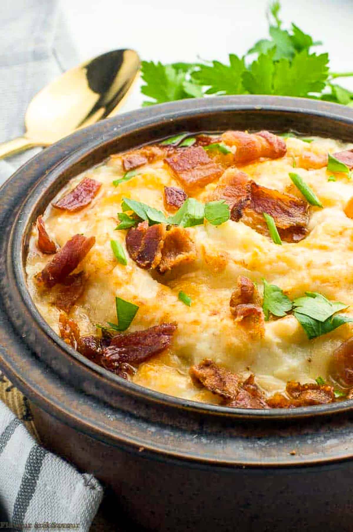 A brown stoneware bowl with mashed  cauliflower, cheese and bacon.
