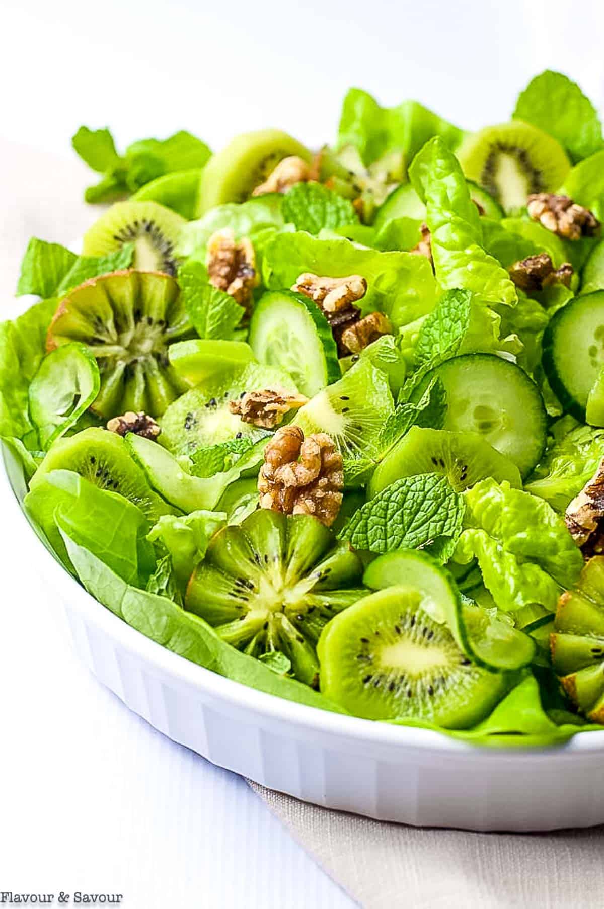 Close up view of kiwi cucumber green salad with walnuts and fresh mint leaves.