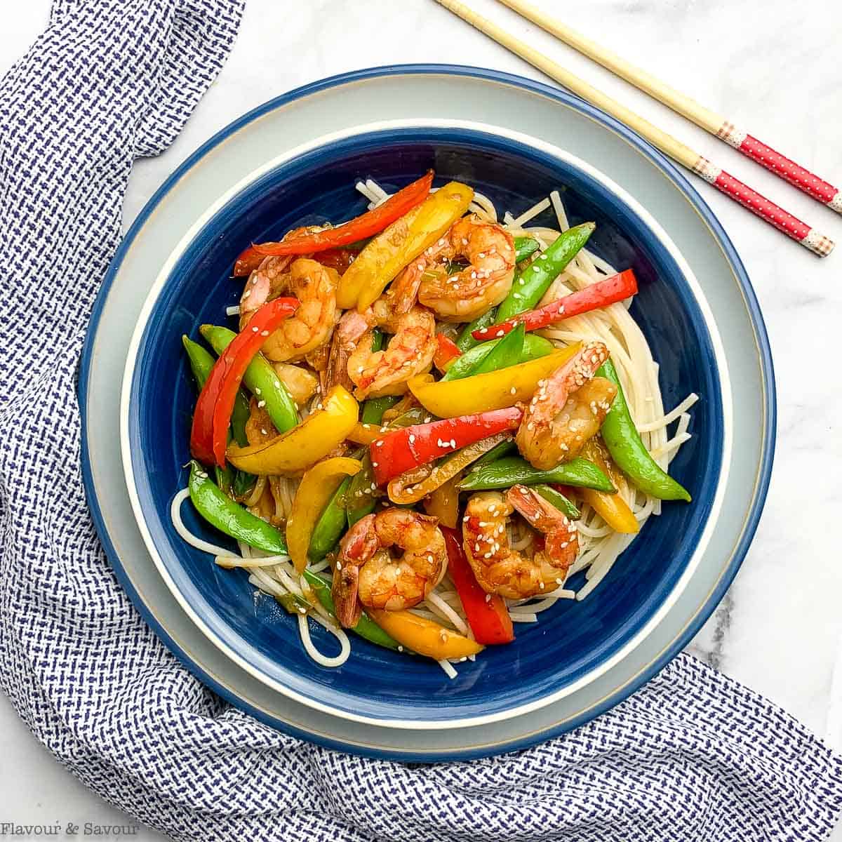 overhead view of a bowl with shrimp and sugar snap pea stir fry on noodles
