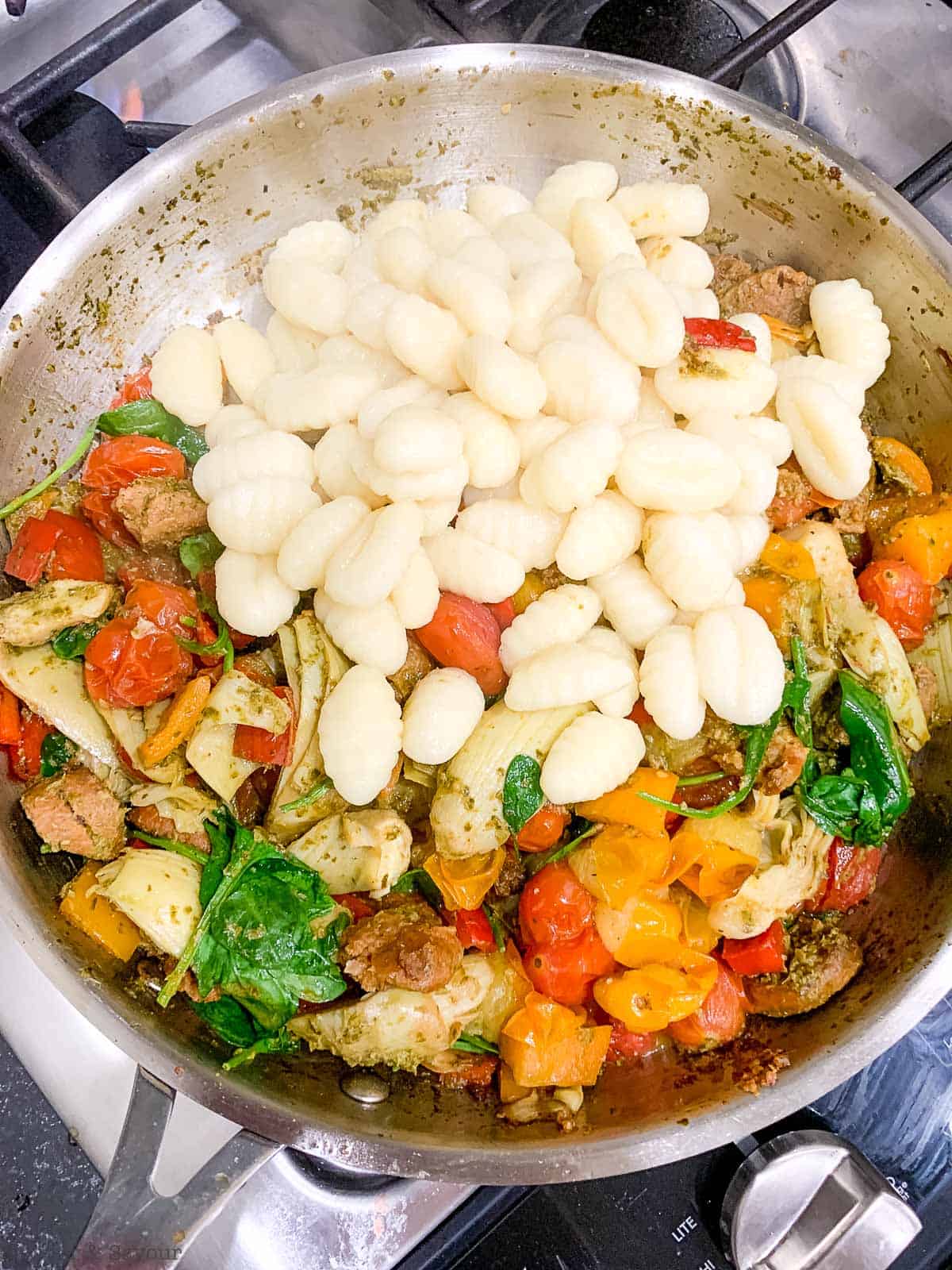 Adding cooked gnocchi to pesto gnocchi in a skillet.