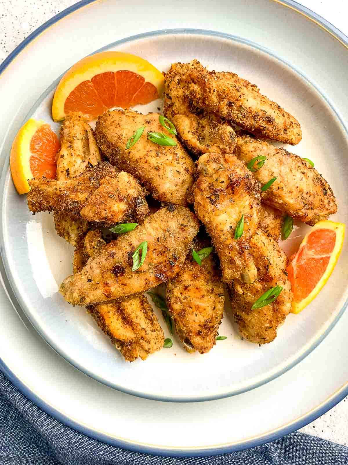 An overhead view of Cajun chicken wings on a plate with orange slices.