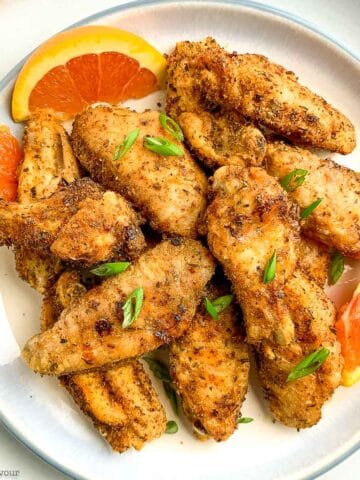 A round plate piled with crispy Cajun chicken wings with orange slices