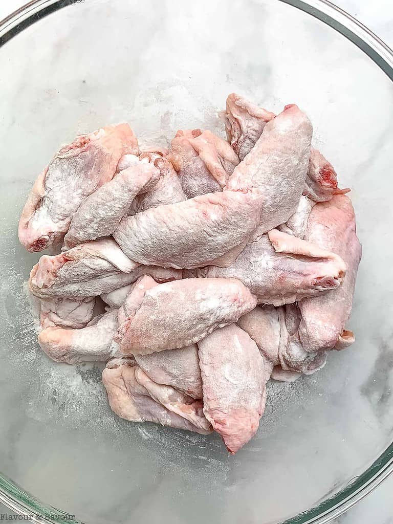 Raw chicken wings in a bowl with baking powder, salt and pepper.