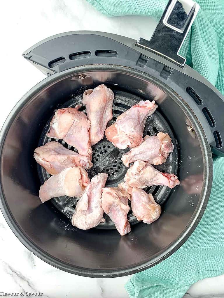 Raw chicken wings in a single layer in an air fryer basket.