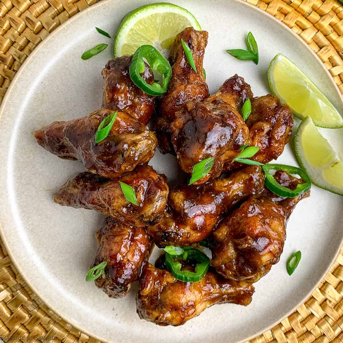 A round plate with 10 jerk chicken wings with lime slices.