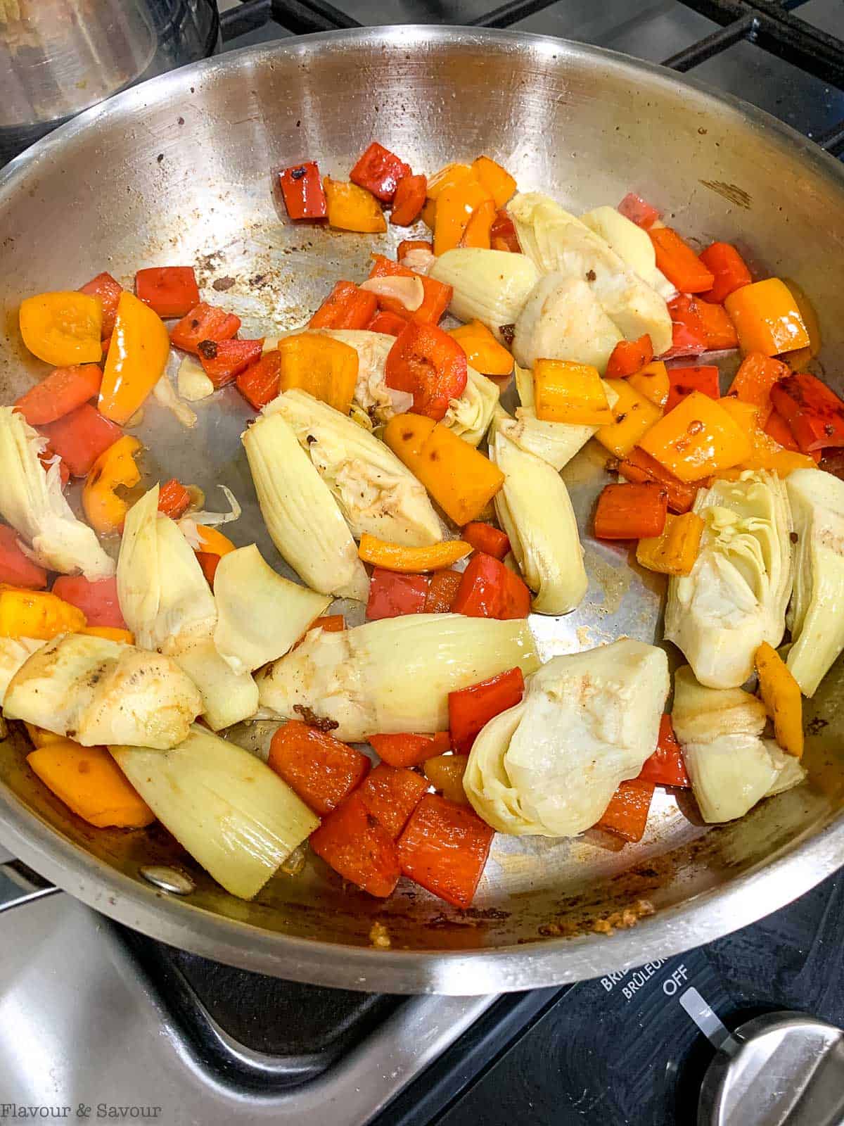 Red bell peppers and artichokes in a skillet.