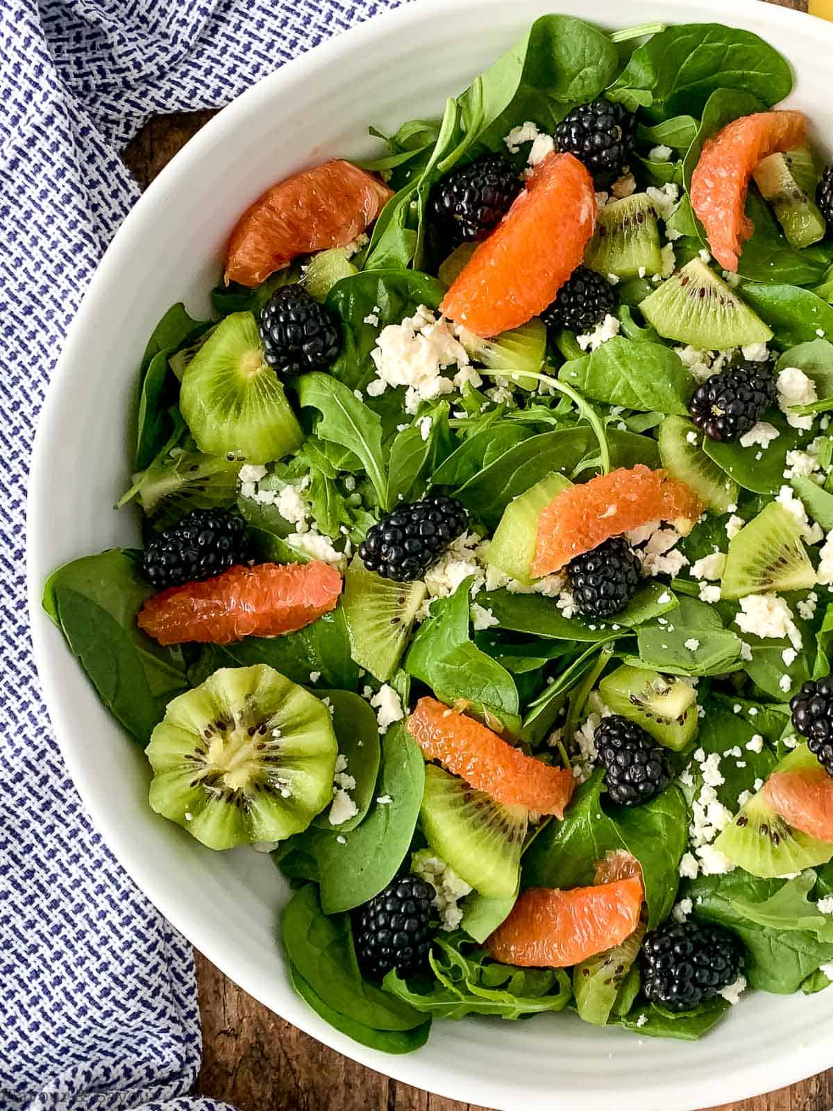 close up view of a spinach arugula salad with kiwi, blackberries and Cara Cara oanges.