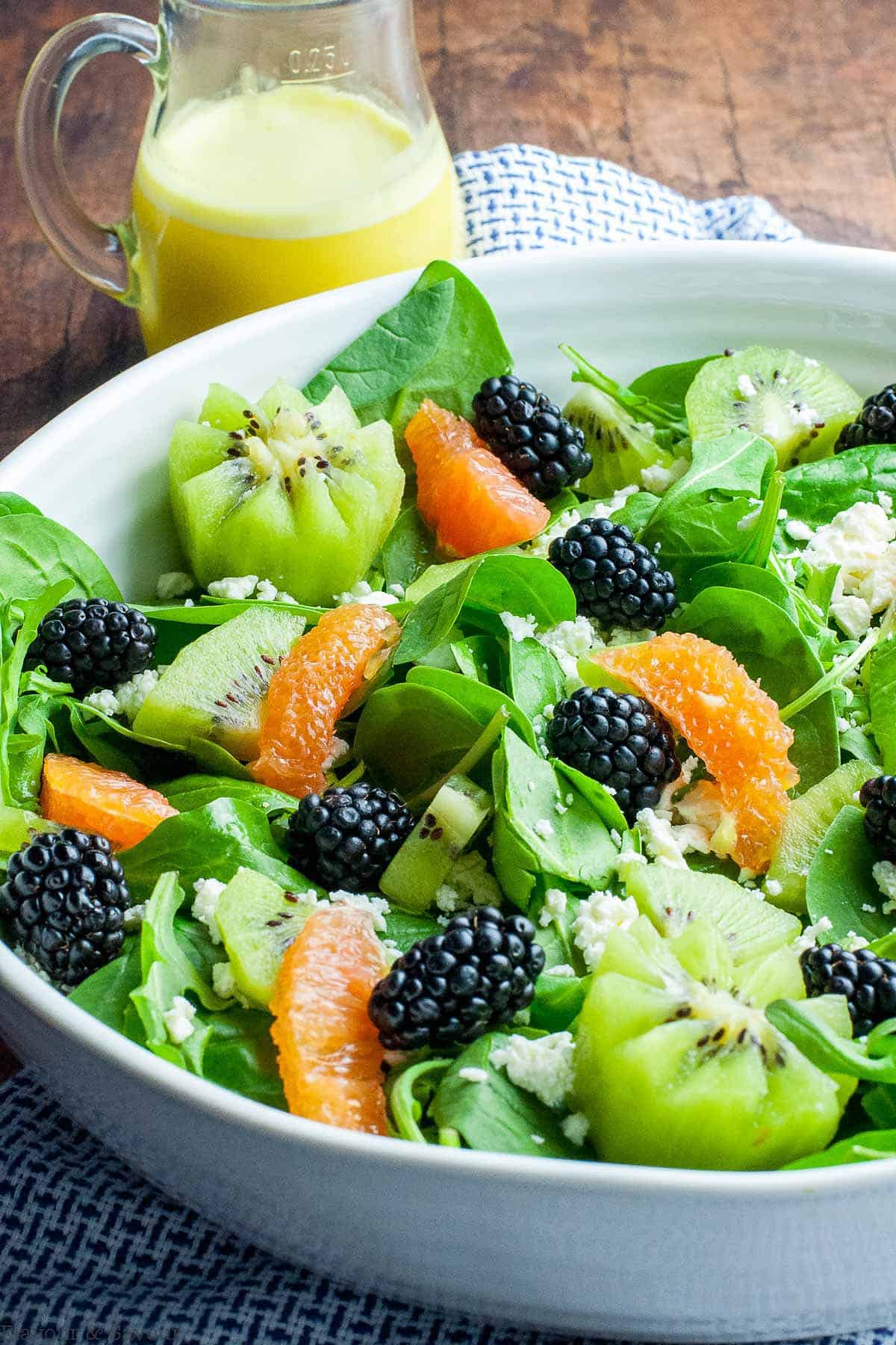 A salad of spinach and arugula leaves with kiwi fruit, blackberries, Cara Cara oranges and feta cheese