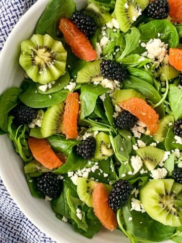 a shallow bowl with blackberry kiwi fruit salad with oranges and feta cheese