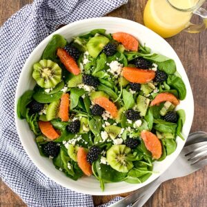 blackberry kiwi fruit salad with oranges with a pitcher of dressing