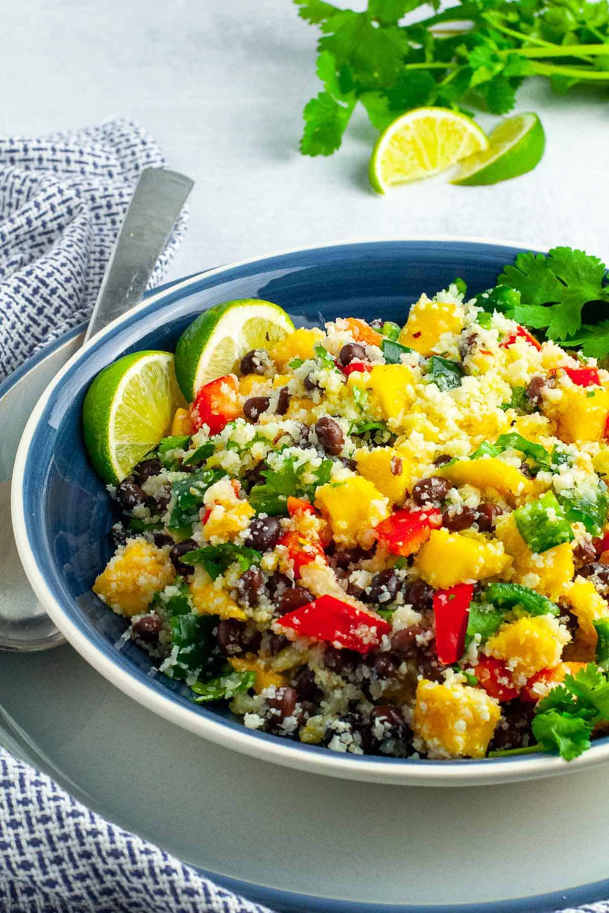 A large blue bowl filled with Caribbean Cauliflower Couscous Salad with lime slice and cilantro leaves.