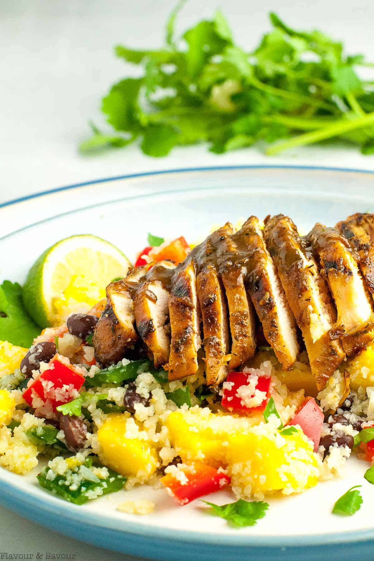 A sliced jerk chicken breast on a cauliflower couscous salad.