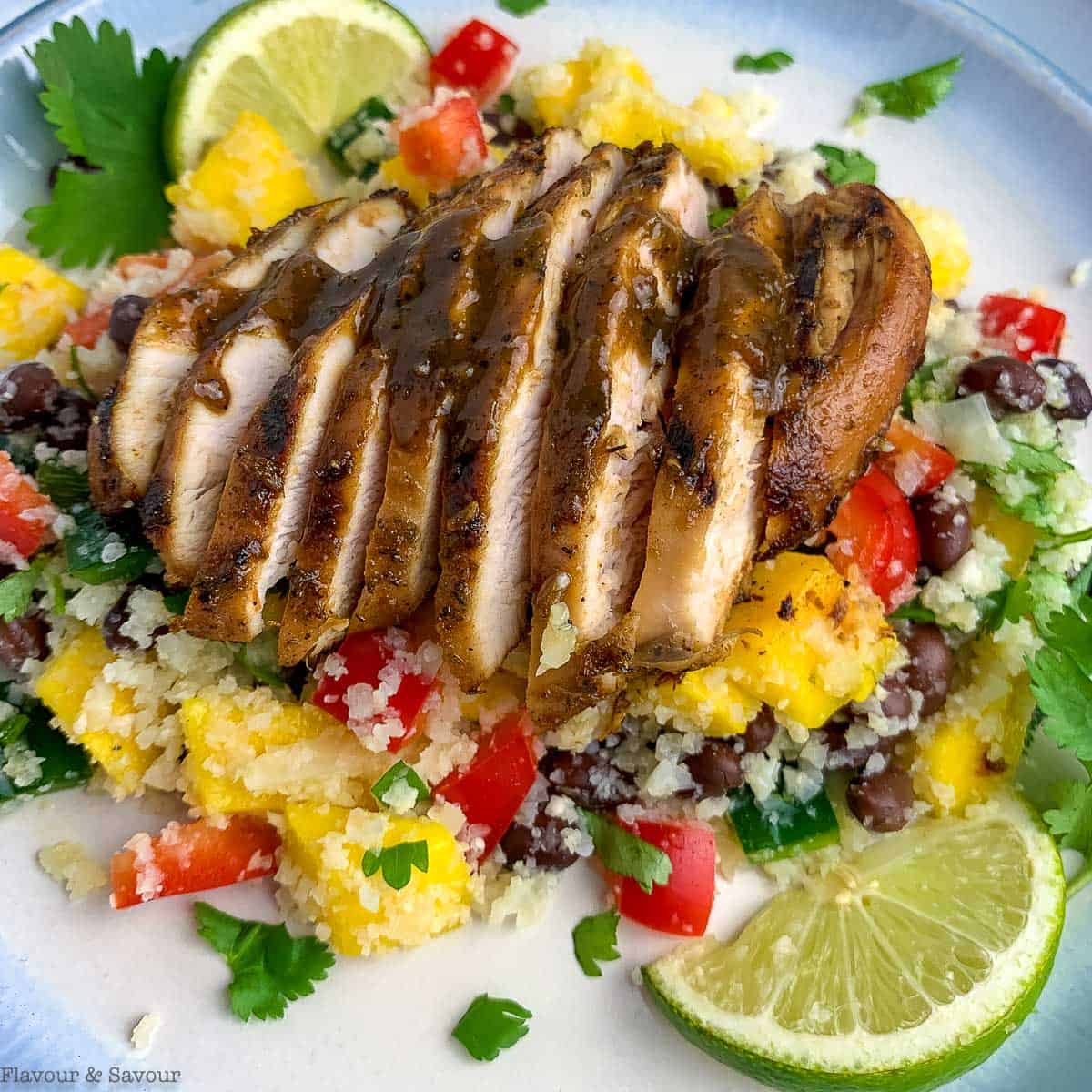 Close up view of a sliced chicken breast with jerk seasoning on a mango black bean couscous salad.