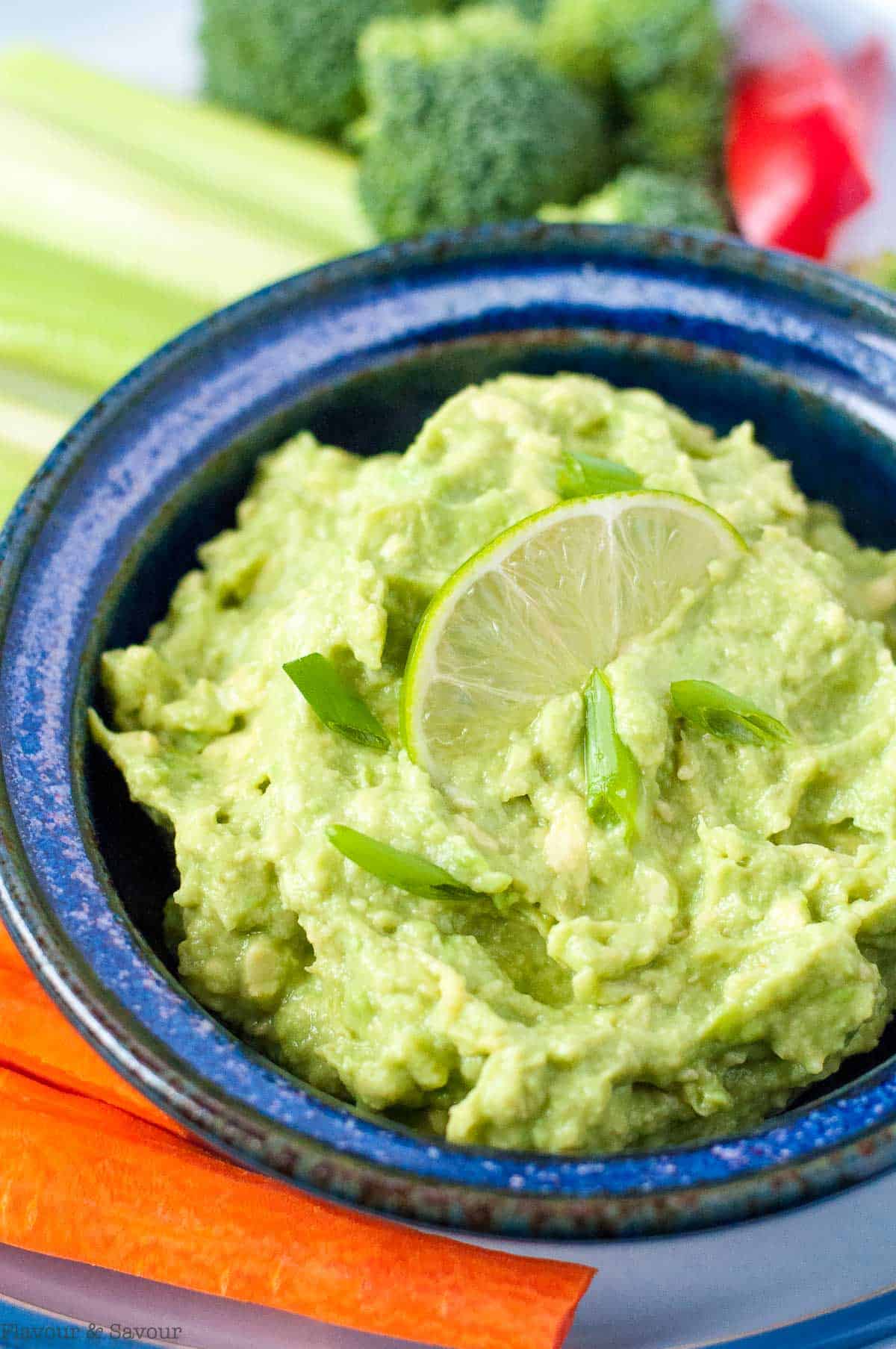 A bowl of guacamole with lime slices and fresh veggies.