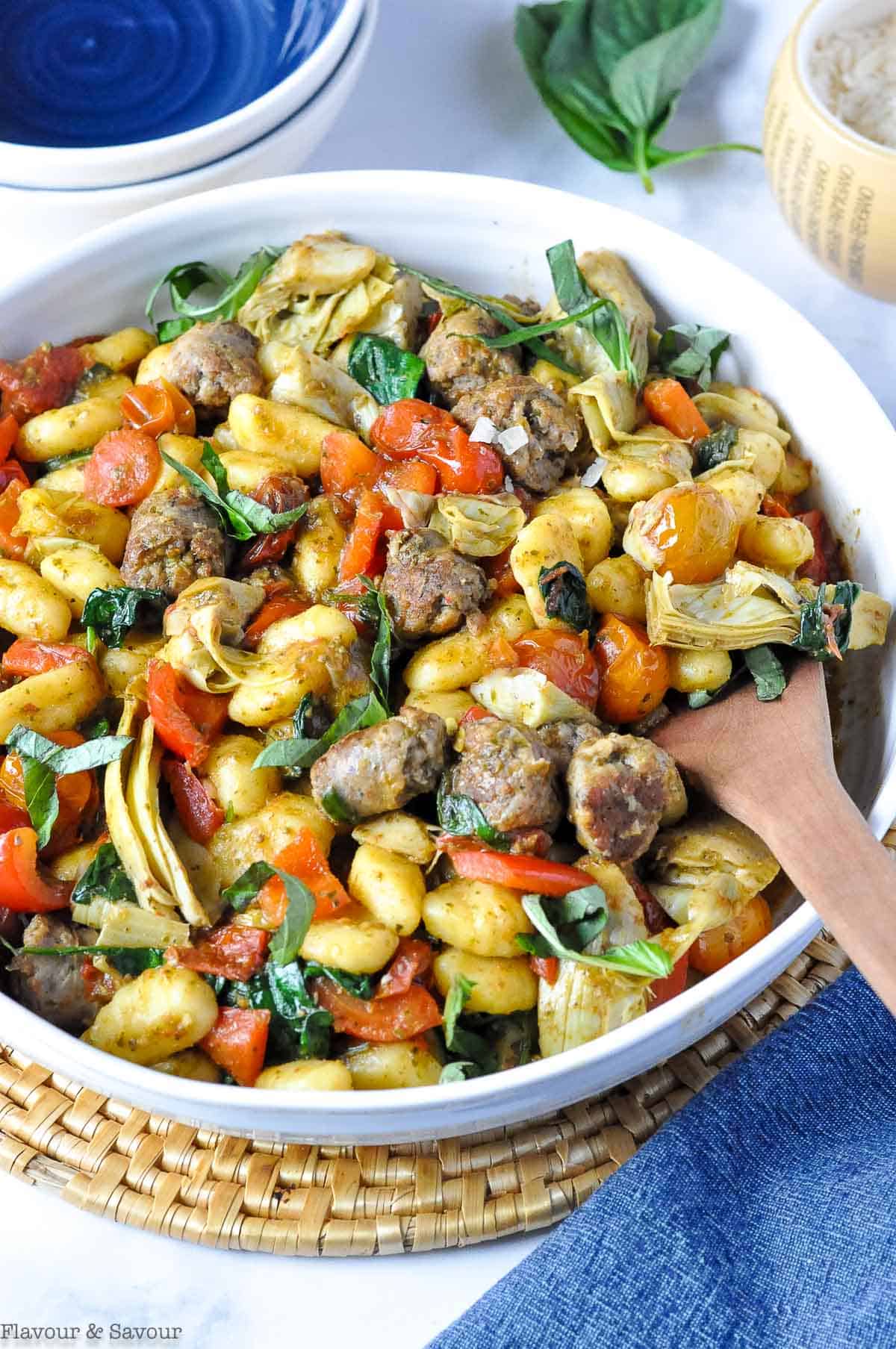 A large bowl with vegetarian pesto gnocchi with a serving spoon