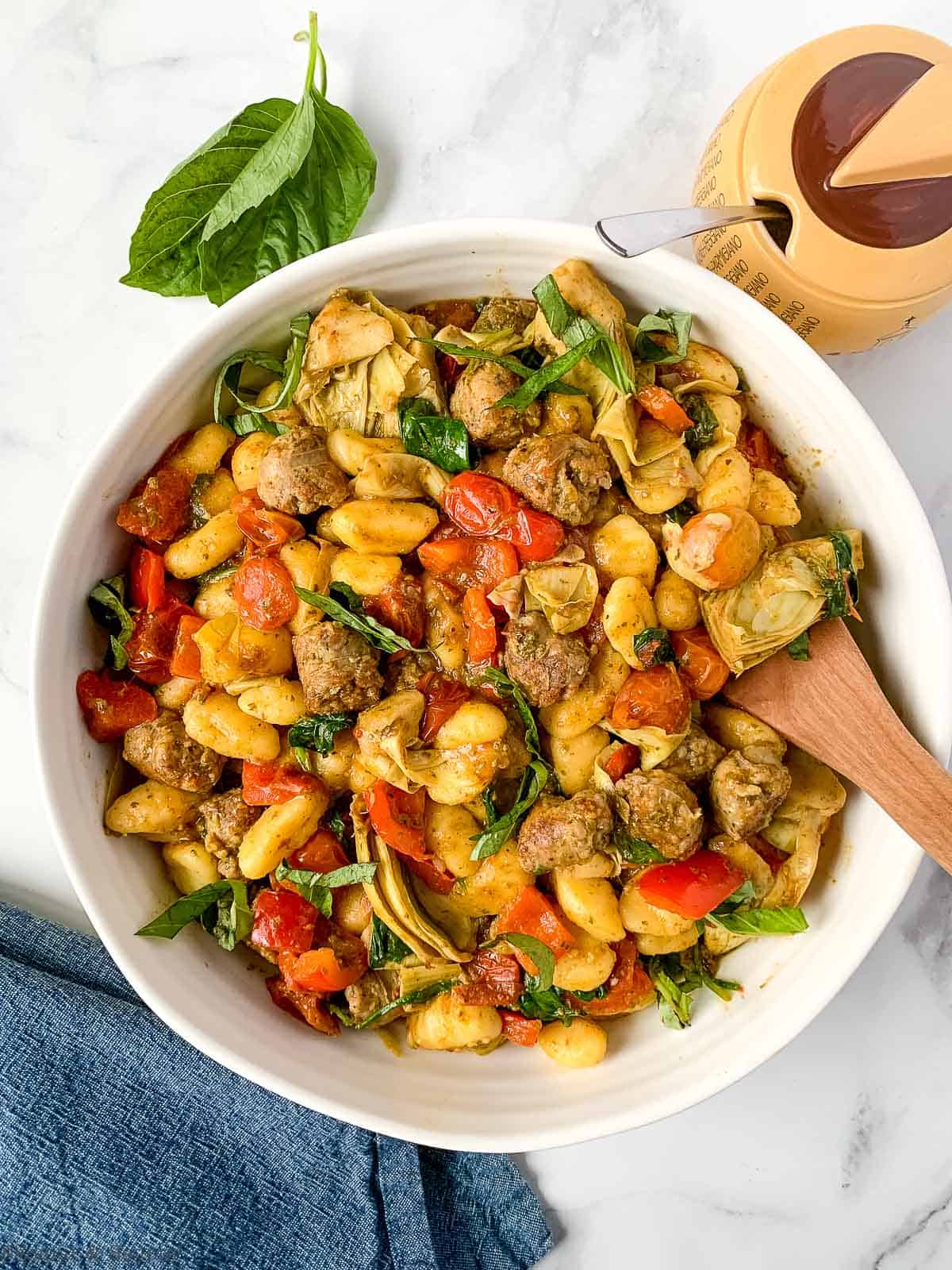 overhead view of a bowl of vegetarian pesto gnocchi with tomatoes, spinach and plant-based sausage.