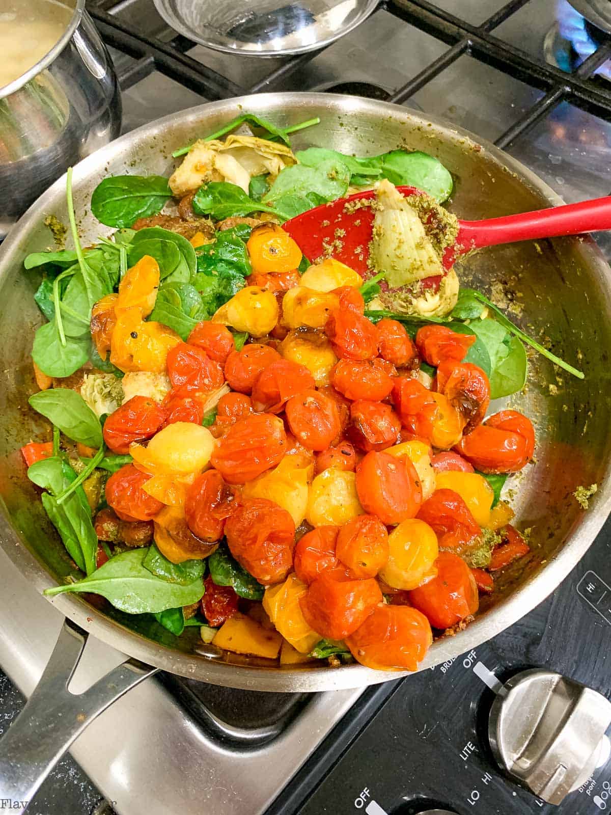 Pesto, spinach and roasted tomatoes in a skillet.