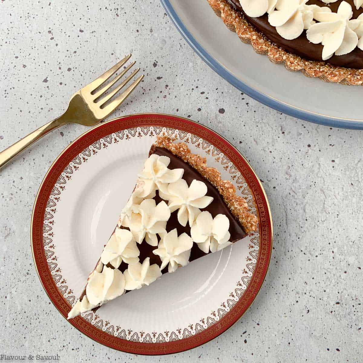 A slice of chocolate ganache tart on a plate with a fork.