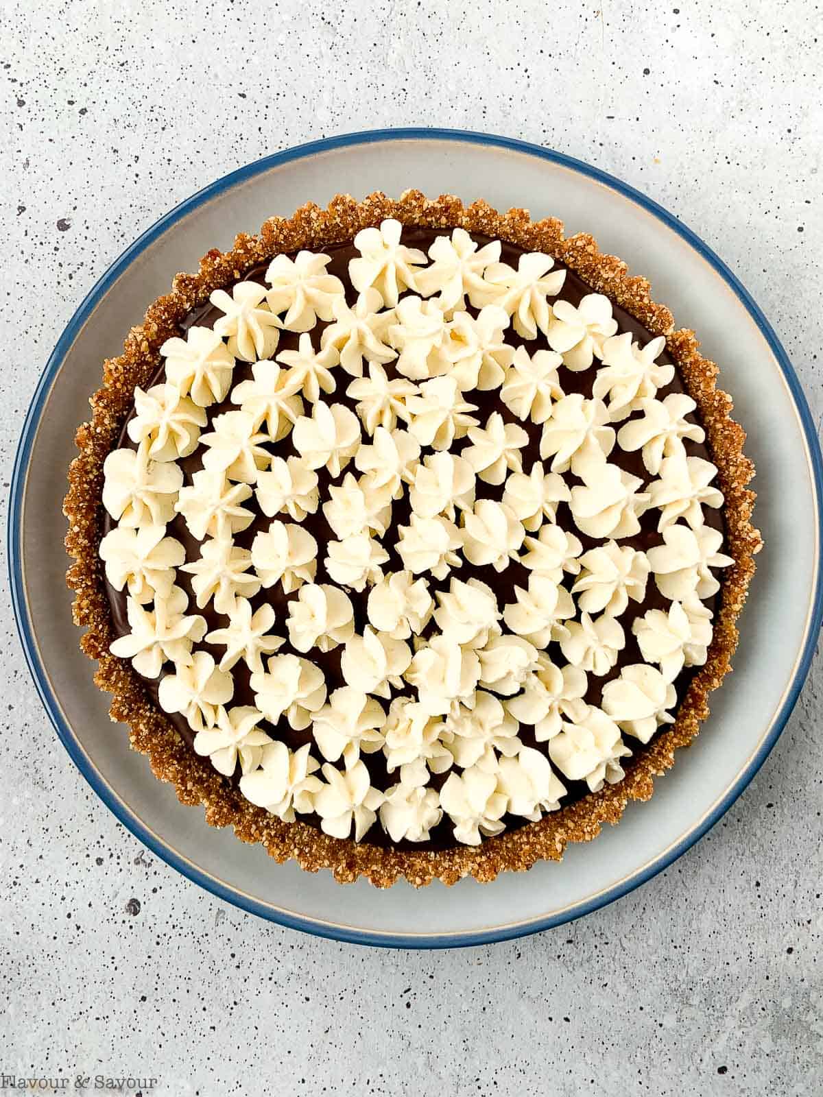 Overhead view of a chocolate ganache tart topped with piped whipped cream.