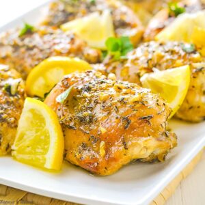 baked lemon chicken thighs on a platter with lemon wedges