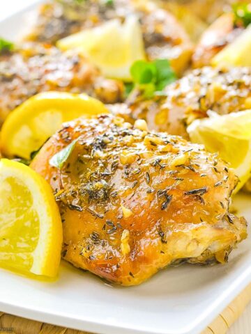 baked lemon chicken thighs on a platter with lemon wedges