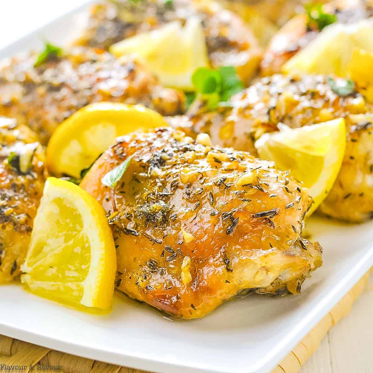 Baked lemon chicken thighs on a platter with lemon wedges.