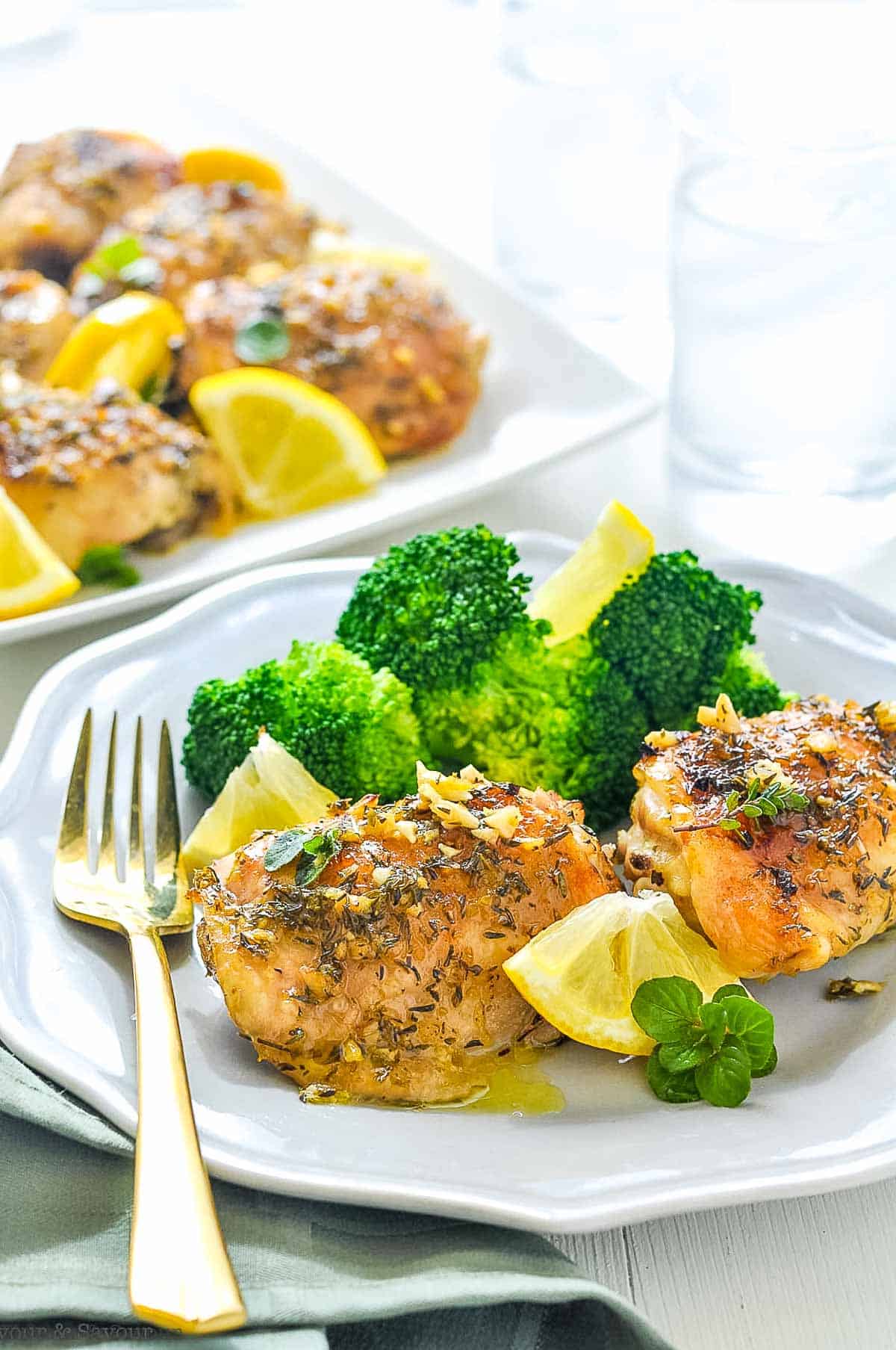 Baked Lemon Chicken thighs on a plate with broccoli and lemon wedges.