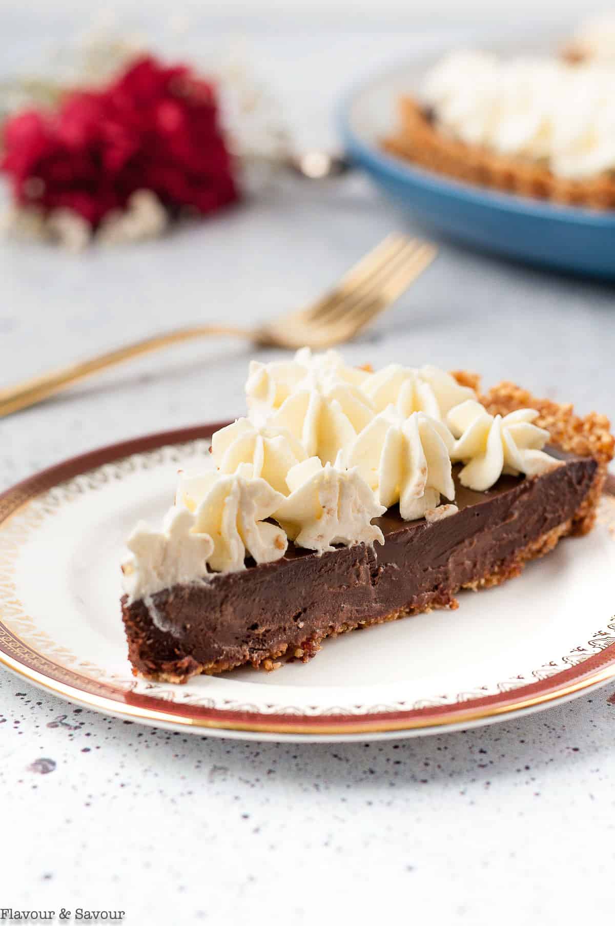 A slice of chocolate ganache tart with whipped cream on a plate.