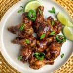 A plate of jerk chicken wings with lime quarters.