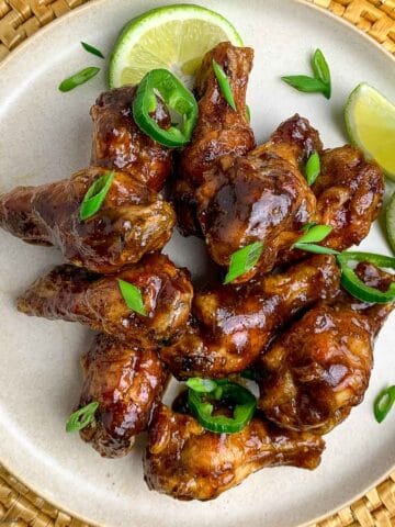 A plate of jerk chicken wings with lime quarters.