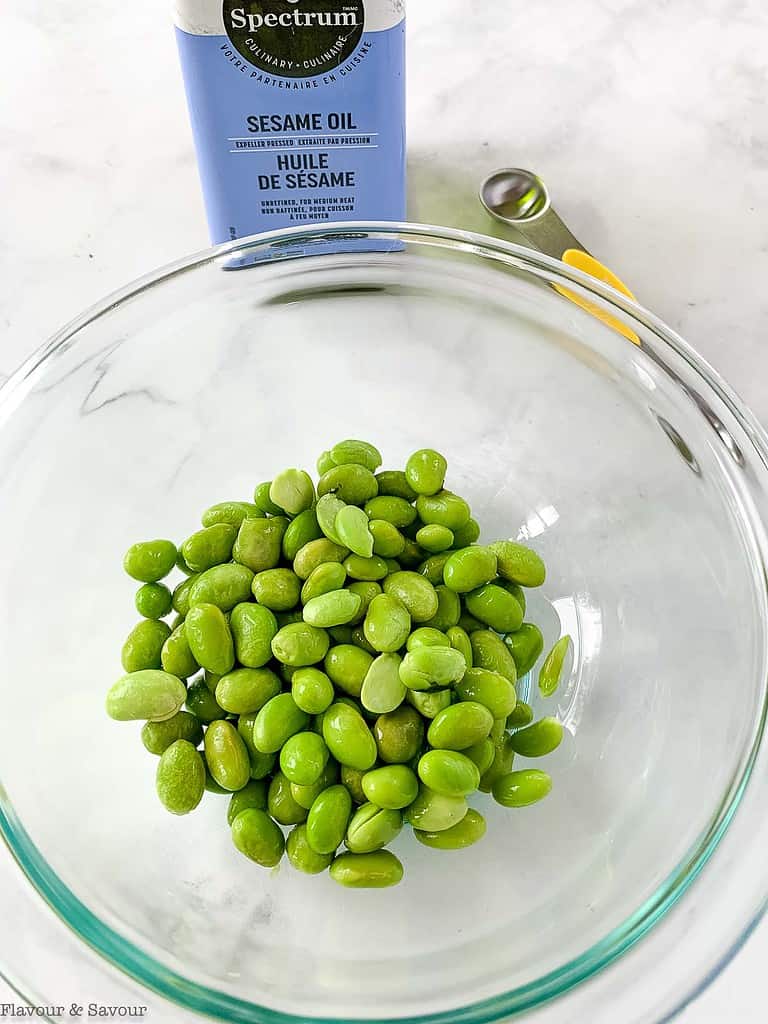 a bowl of edamame with a jar of sesame oil beside