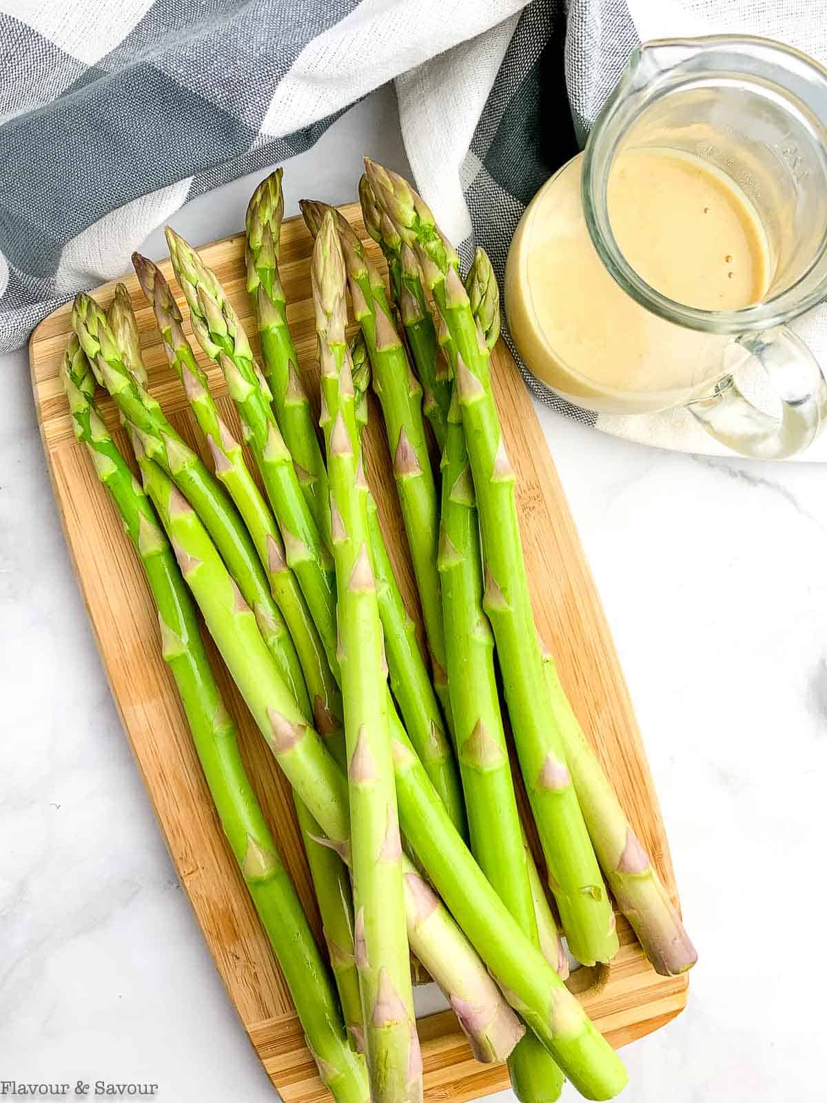 raw asparagus spears and a small jug with lemon tahini sauce