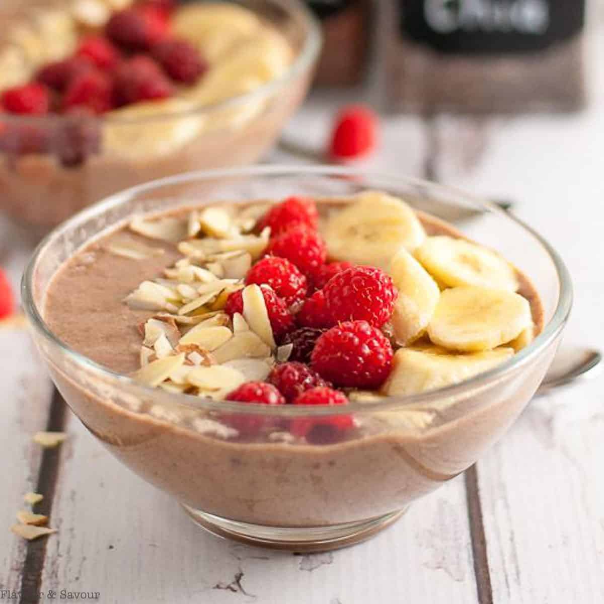 close up view of a smoothie bowl garnished with raspberries, banana slices and flaked almonds