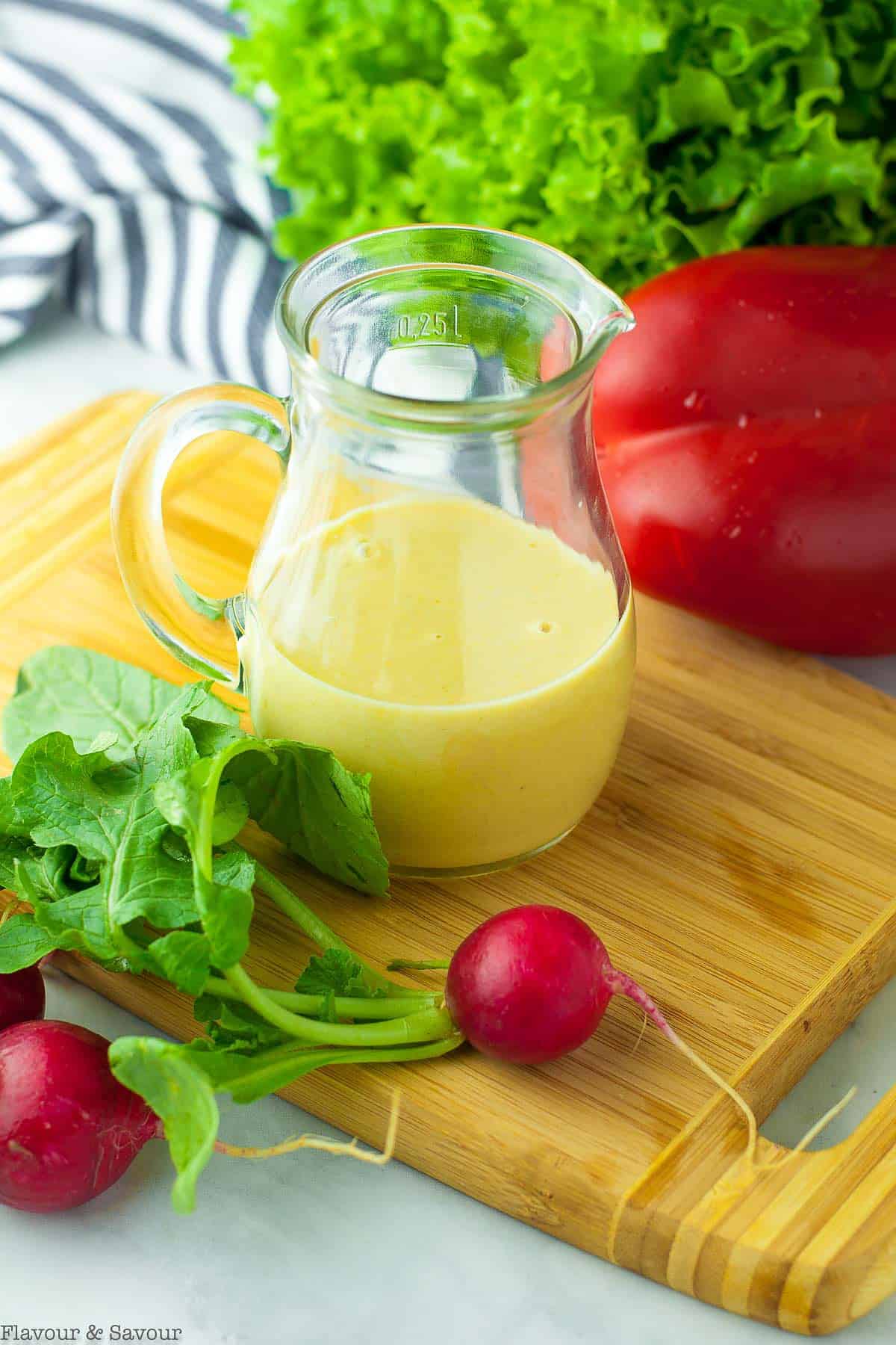 Lemon Tahini Dressing in a small pitcher surrounded by fresh salad vegetables