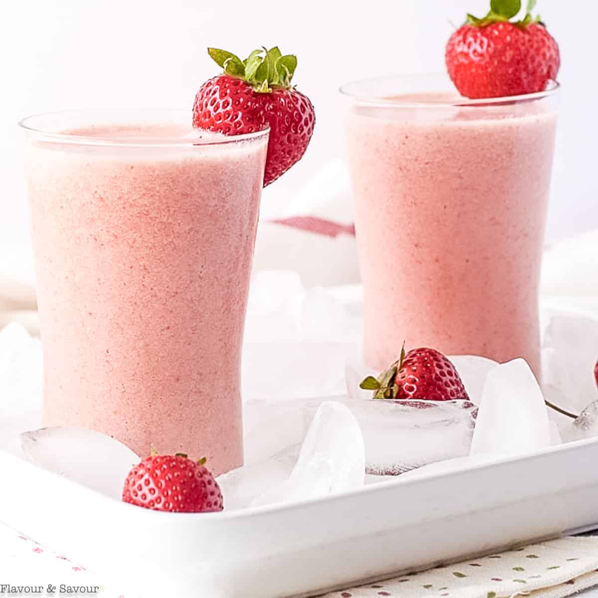 Two tall glasses of strawberry watermelon collagen smoothie topped with fresh strawberries.