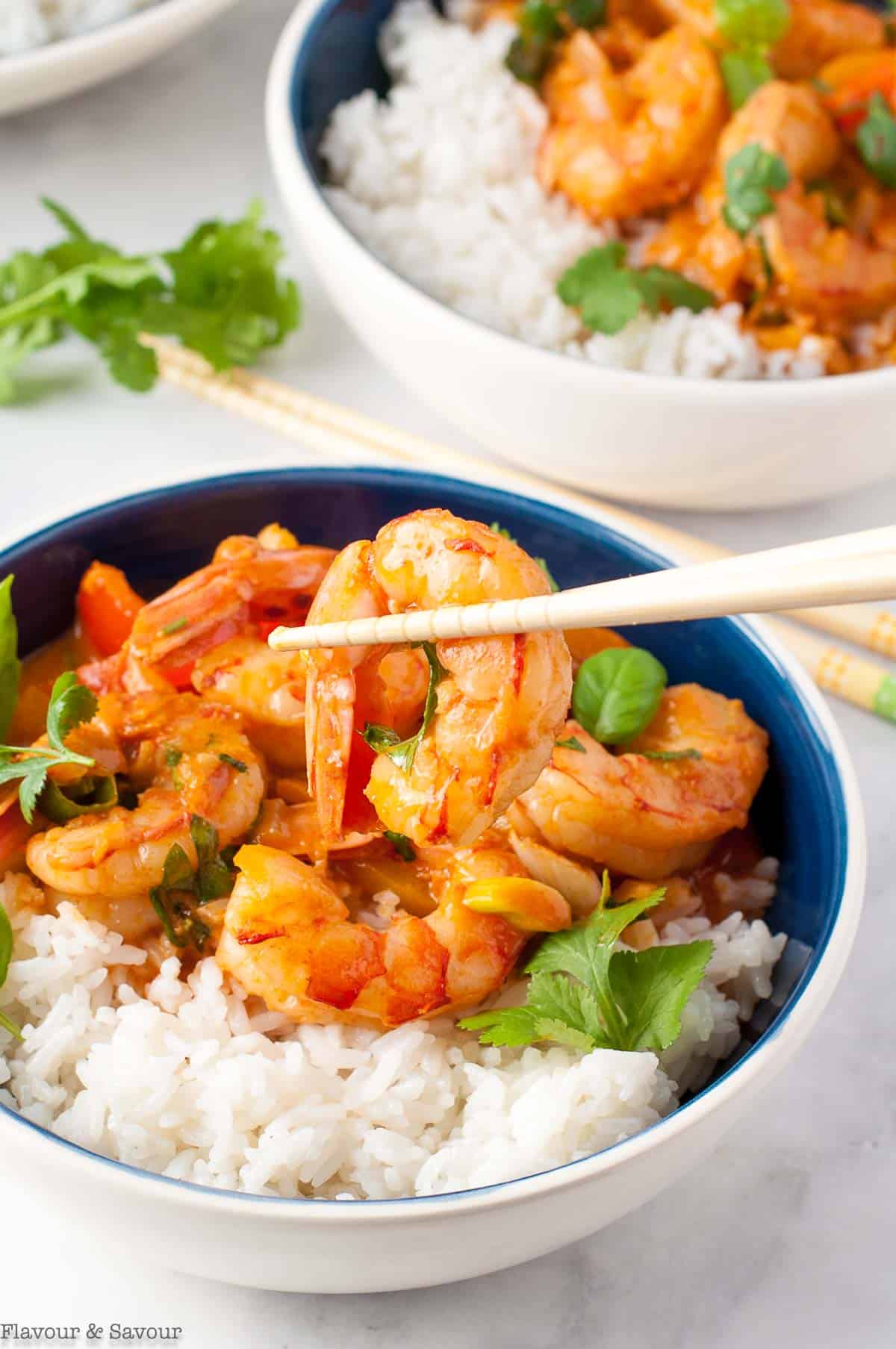 Thai red curry with shrimp lifted up with chopsticks.