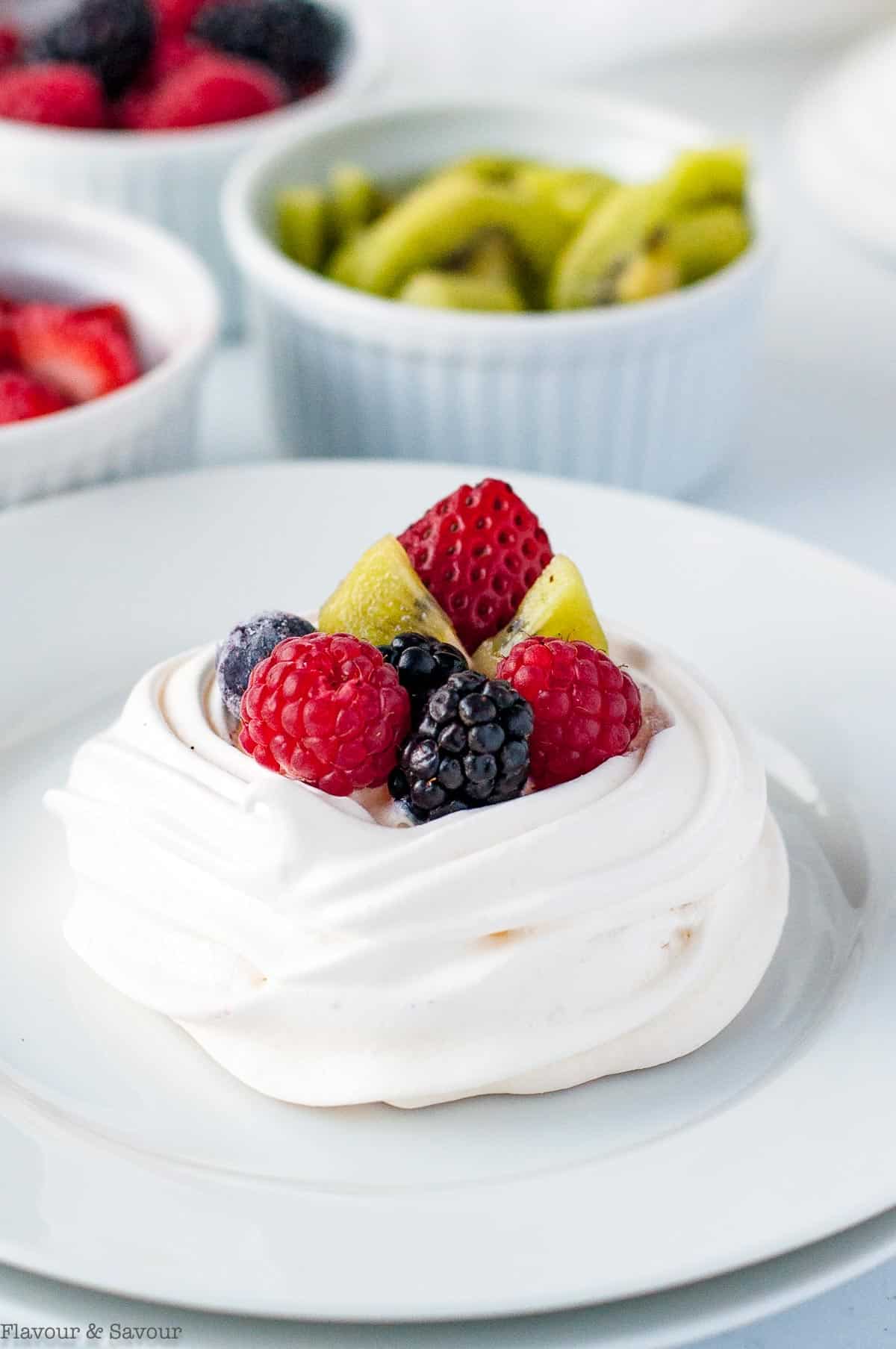 Close up view of a mini pavlova nest topped with fresh berries and kiwi.
