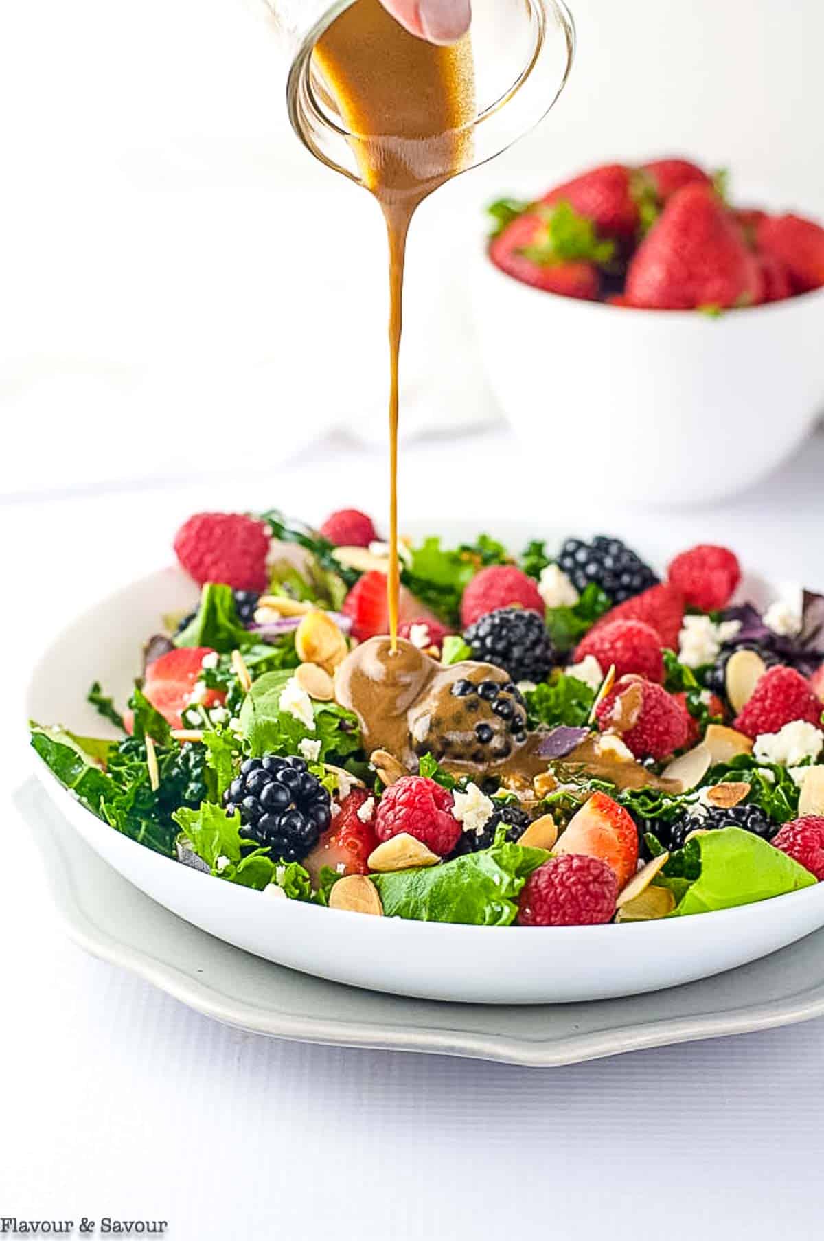pouring balsamic dressing on mixed green salad with berries