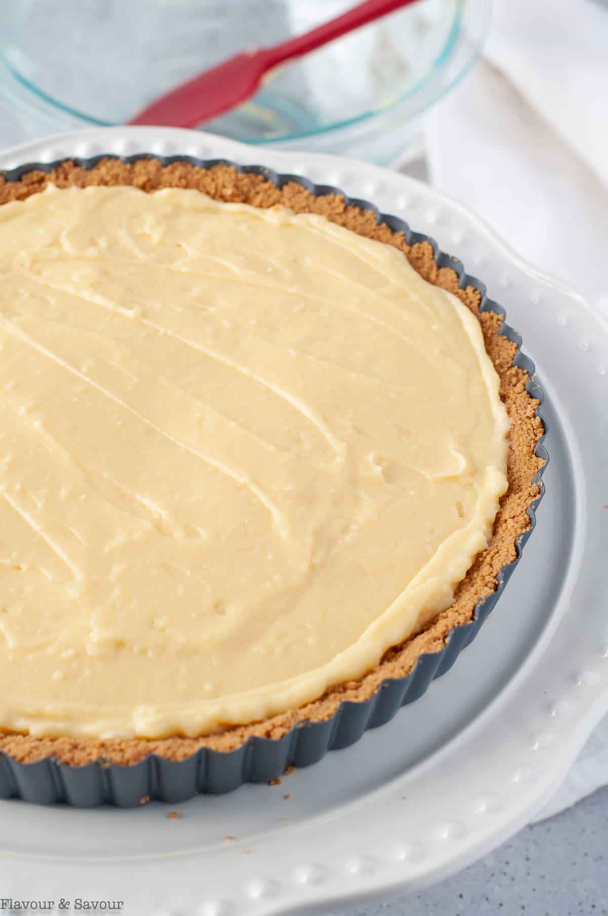 Adding vanilla pastry cream filling to a gluten-free graham cracker crust in a tart pan with a removable bottom.