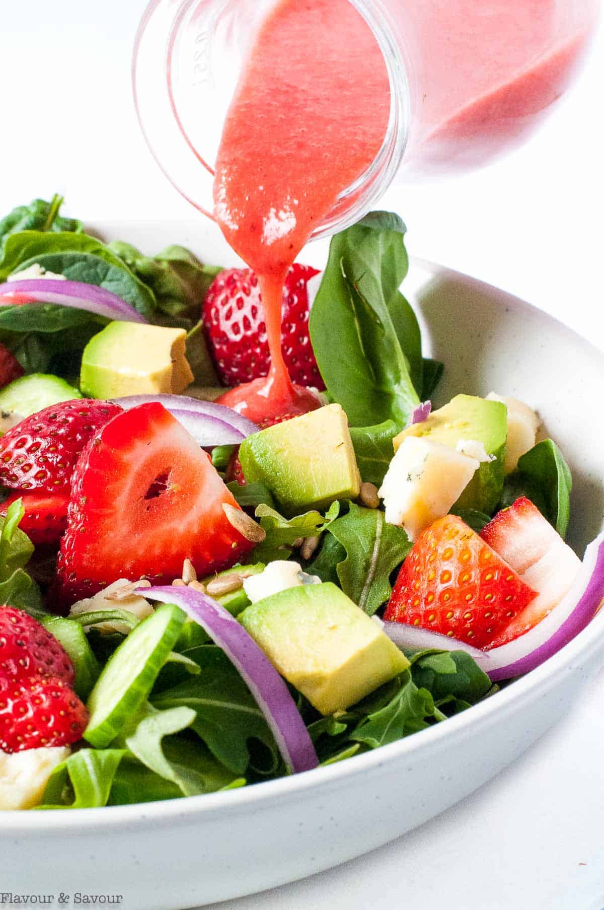 Pouring strawberry vinaigrette on strawberry spinach salad.