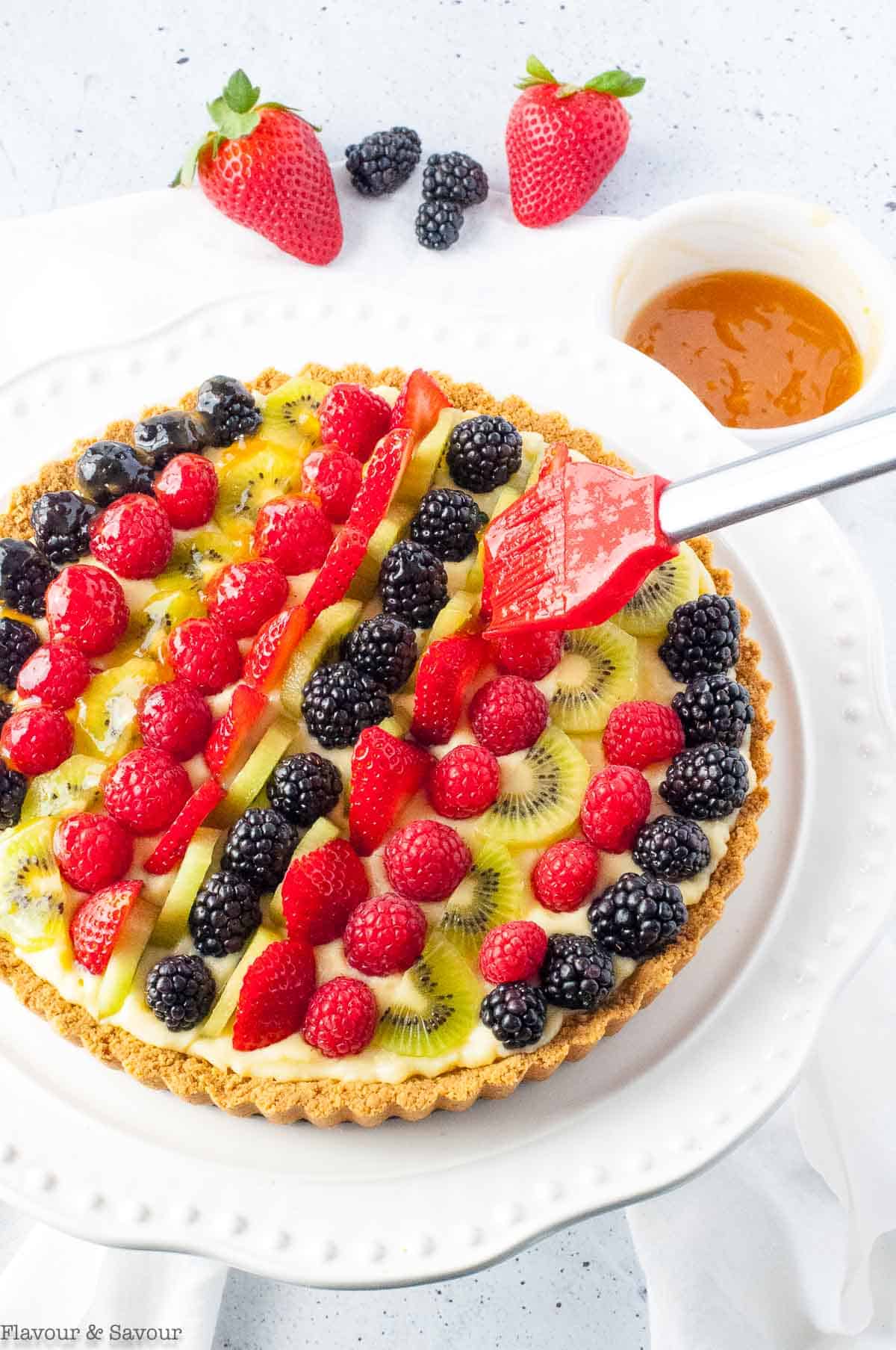 Brushing apricot glaze on fruit tart with a pastry brush.