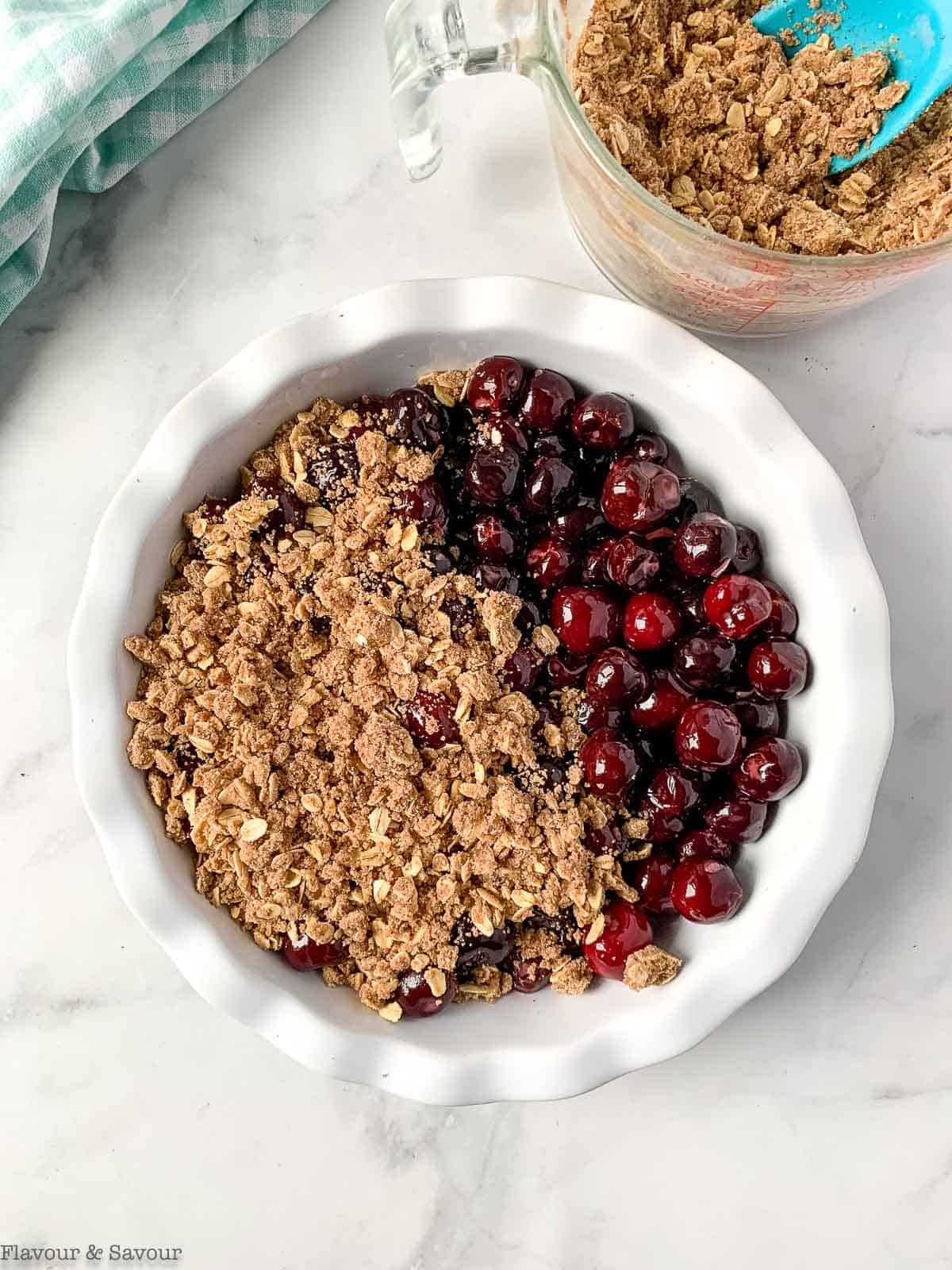 Adding crumble topping on top of cherries in a round baking dish.