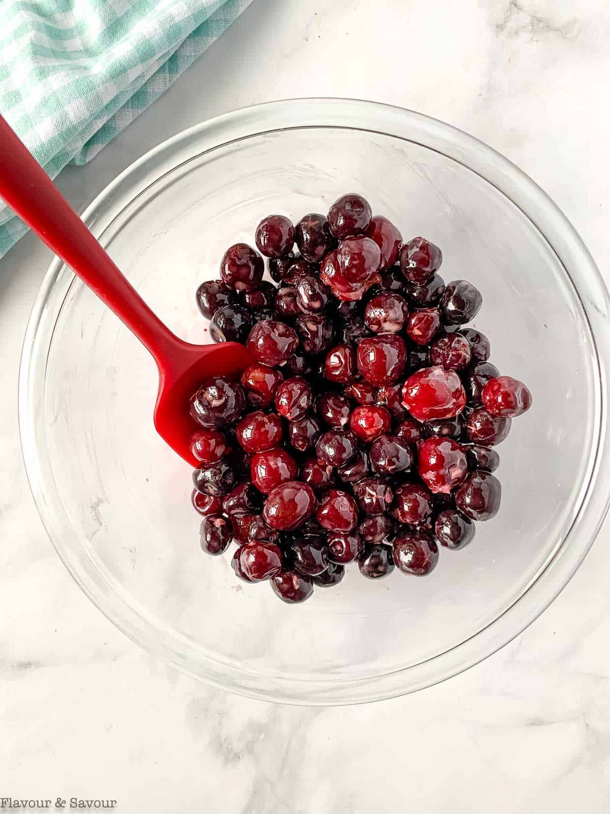 Cherries for cherry crisp in a glass bowl with a spatula.