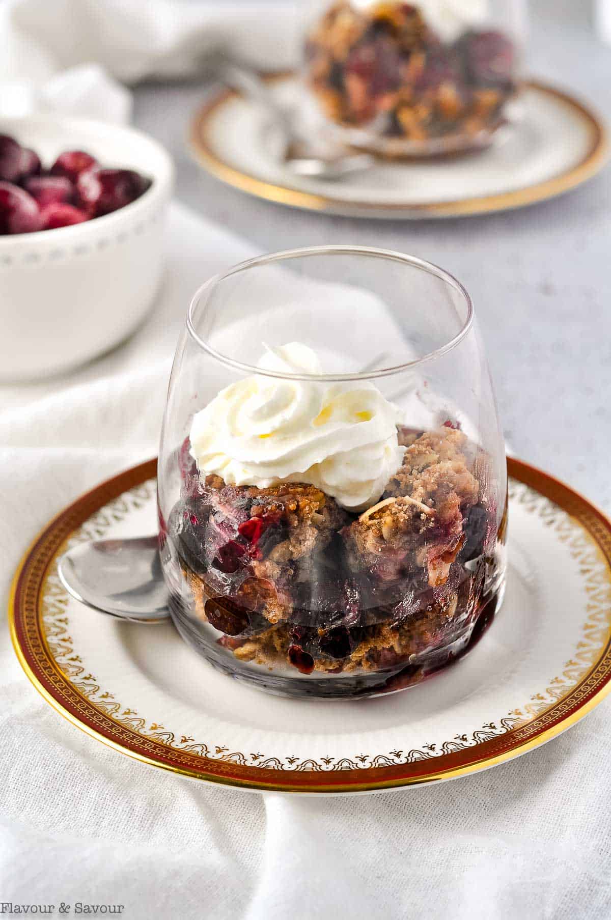 cherry crisp made with frozen cherries in a dessert glass with whipped cream.