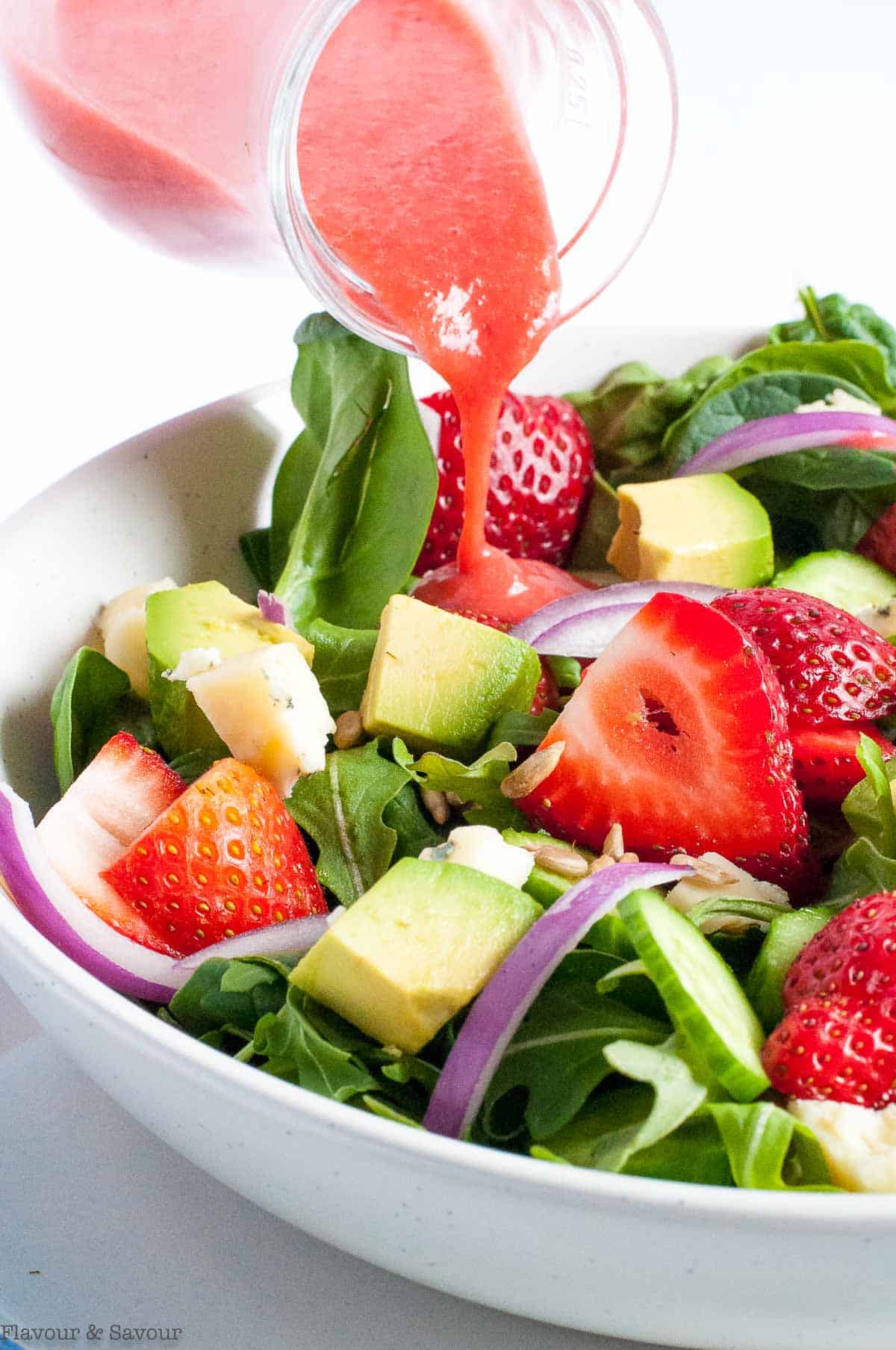 Adding strawberry vinaigrette to a strawberry salad.