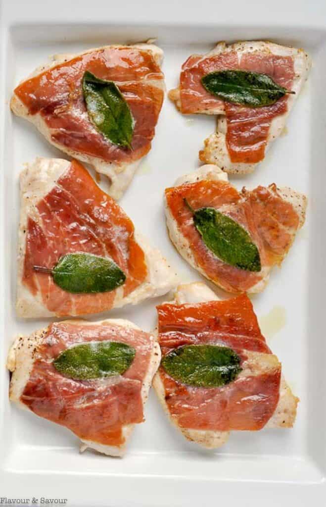 Chicken breasts wrapped in prosciutto with a sage leaf pressed on top.