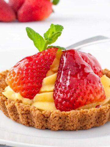 Strawberry tart with pastry cream, fresh sliced strawberries and a mint leaf.