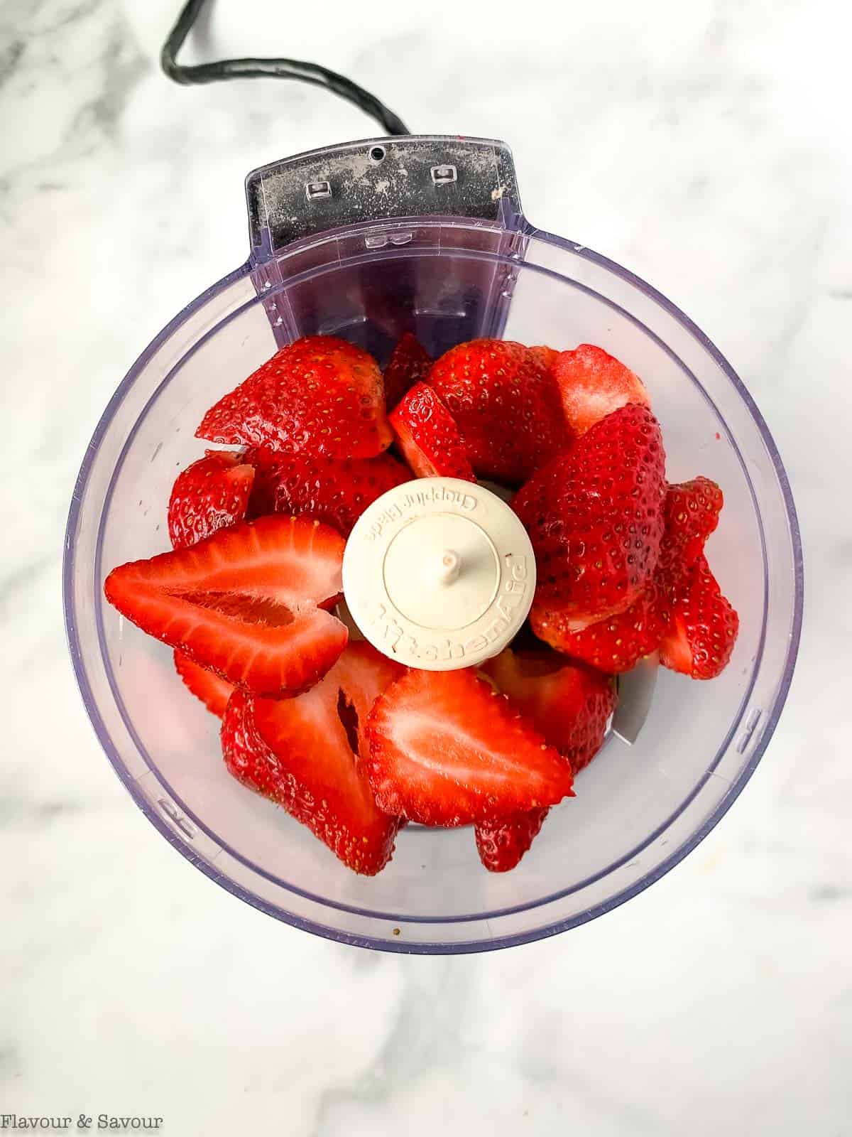 Sliced strawberries in the bowl of a food processor.