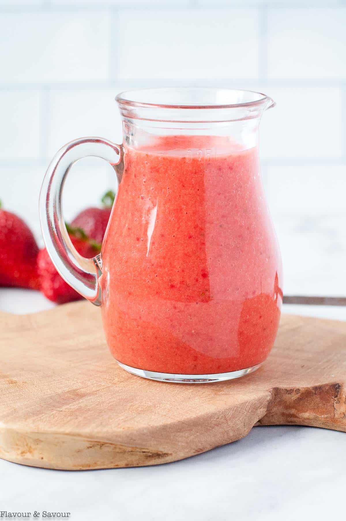 A small pitcher of strawberry vinaigrette on a wooden board.